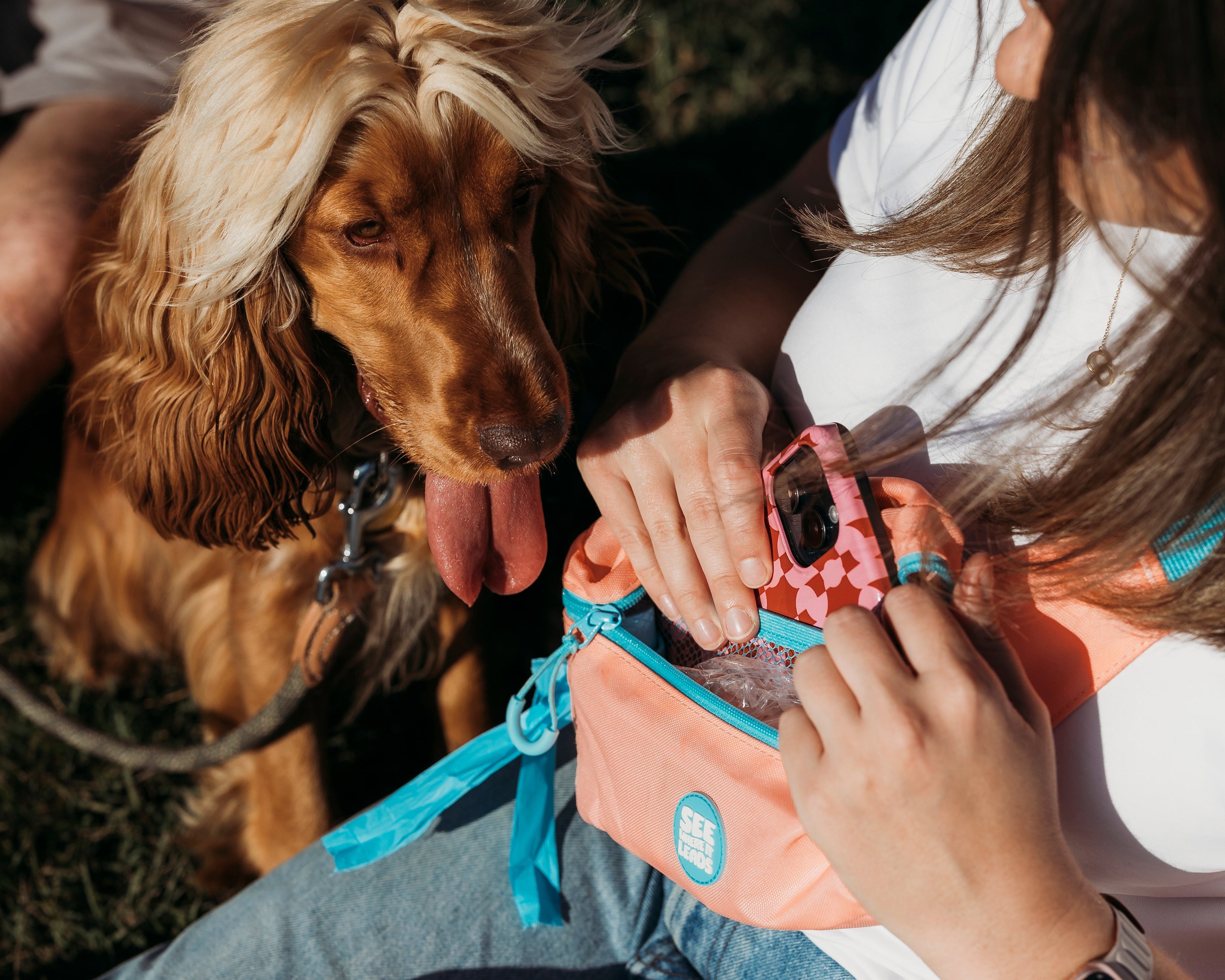 Person (Sophie) sitting outdoors with a Cocker Spaniel dog (Pearl), holding a See Where It Leads Goodie Bag in Pink.